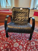 Front view of a black leather armchair with wooden bent frame and armrests, showing the seat and back cushions with wrinkled leather.