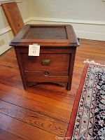 Closed view of the antique child's wooden commode showing its dark stained wood and original hardware.
