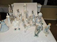 Full view of seventeen assorted porcelain figurines including some identified as Lladro, showing various poses and sizes on a table.