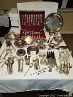 Photo of two 12-piece silver-plate flatware sets, boxed and unboxed; various silver-plate serving utensils and pieces including tray, bowls, candy dishes, coasters, and decorative frame