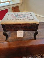 Photo of antique footstool showing embroidered fabric lid with floral needlepoint design on carved wooden frame with cabriole legs