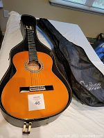 Full view of Aria AK-20 classical guitar in black hard-shell case with soft sleeve.