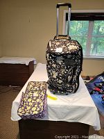 Vera Bradley rolling duffle bag standing on table with telescopic handle extended, Amy Butler Toiletry Kit laid flat next to it