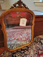 Full front view of maple wood framed antique mirror with carved crest and shaped wooden frame reflecting interior.