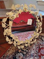 Front view of a round mirror framed with cream-colored wrought iron leaves and flowers, showing vintage floral design and condition.