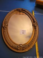 Framed oval mirror with ornate gold frame and decorative detailing, measuring approximately 24 inches. Minor cosmetic blemishes visible on frame.