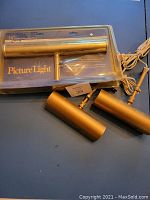 Three gold-colored picture lights. One new in packaging, two used out of package.