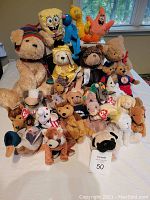Photo showing approximately 28 plush toys including recognizable characters Spongebob Squarepants and Patrick Star, along with multiple Ty Beanie Babies and other animal plush toys arranged on a bed.