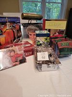 Photo showing brass desk lamp, beer brewing kit, Princess Diana 1998 calendar, LED spotlight, corkscrew, holiday hand towels, boxed museum notecards, Martha Stewart cookbook, and ceramic travel mug all arranged on a surface.