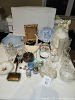 Wide shot of lot containing porcelain tray, crystal figurines, silver lotus bowl, porcelain bowls, crystal clocks, picture frames, and assorted decorative items