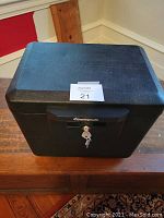 Closed black Sentry fireproof safe with key in lock, placed on wooden surface.