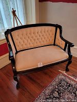 Front angle view of tufted settee with black wood frame and cream upholstery