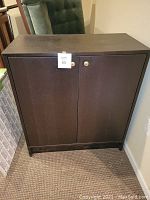 Brown 2-door wooden storage cabinet with keyhole and minor wear.