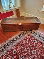 Closed antique storage chest showing oak framed panels and wood grain with small lot number attached to front center