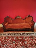 Front view of the 19th century camelback sofa in orange velvet with carved wooden frame and two matching bolsters.