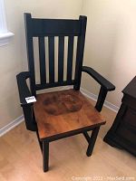 Front view of the wooden armchair showing black frame and natural wood seat, some wear visible.