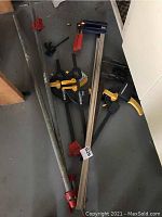 Photo showing 8 various clamps on floor, including pipe clamps, bar clamps, and plastic quick-release clamps