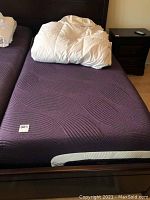 Purple mattress on adjustable bed frame with headboard and side rails visible