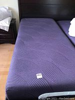 Purple mattress on dark wood headboard frame, showing surface texture and condition
