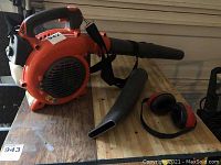 Full view of blower main unit, detachable nozzle, shoulder strap, and ear protection on wooden surface