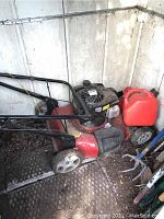Red Briggs and Stratton 500 series gas lawn mower with some rust and dirt, shown from side angle in a storage area with nearby gas container
