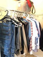 Closet view showing hanging men's pants, shirts, and belts.