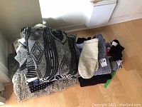 Folded men’s sweaters piled showing various colors and textures with socks on the side.