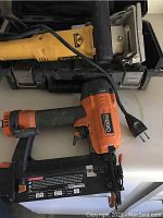 Ridgid brad nailer and DeWalt plate joiner tools placed side by side on a table with DeWalt black carrying case visible.