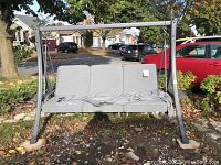 Full view of the three-seater swing on steel frame with cushions and canopy in yard
