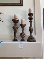 Front view of the three gold gilded and purple turned column candle holders with white pillar candles, arranged by height 12", 16", 20".