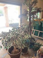 Photo of several artificial palm trees with green leaves in brown plastic pots inside a garage space.