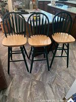 Three wooden swivel bar stools displayed together showing natural wood seats and dark green spindle backs and legs