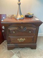 Closed view of one wooden bedside table showing carved details and brass hardware on drawers.