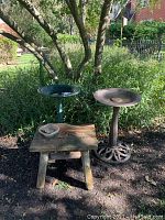Bird baths and wooden table placed outdoors on grass and dirt under a tree, showing the overall condition and size.