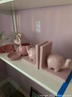 Shelf with pink ceramic elephant bookends and assorted pink ceramic items including pig bowl, ashtray, and flamingo sachet holder.