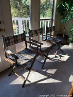 Three folding captain chairs in a row, placed indoors near glass doors showing outdoor deck area.