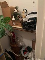 Christmas items stored in a closet shelf and bags, including some trees, boxes, and bags possibly containing decorations and lights.