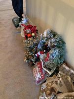 Photo showing Christmas wreath, bags of ornaments, and decorative items aggregated together against a wall.
