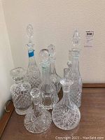 Photo of 8 vintage fine crystal and cut glass decanters with various shapes and sizes, all with stoppers, arranged on wooden surface.