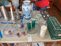 Table setup displaying assorted cut glass dishes, blue and white ceramic vase, crystal globe candle holders, votive candle holders, and boxed white candles.