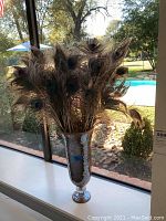 Tall silver mosaic finish vase with a narrow base and wide top, filled with multiple natural peacock feathers.