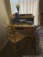 Photo showing full view of desk and chair in front of window, displaying furniture and some decorative ceramic items on desk.