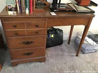 Full front view of wooden student desk showing the attached left-side 3-drawer cabinet and desk surface top with books and decorative items.