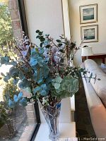 Full view of faux flower arrangement with eucalyptus leaves and pussy willow stems in clear glass vase positioned by window.