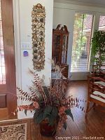 Full view of dried floral and feather arrangement in painted metal vase near wall plaque
