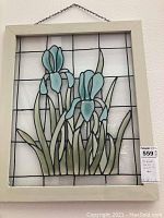 Art Deco stained and leaded glass panel with iris flower design in blue and green hues within a white frame hung by a chain.
