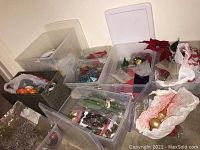 View of bins and containers filled with assorted holiday decorations including ribbons, ornaments, dried flowers, and wreath hangers.
