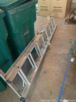 Side view of the folded aluminum ladder showing length and rungs, placed next to green bins.