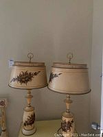 Pair of vintage L. Hitchcock metal lamps with hand-painted floral designs on bases and shades, shown side by side.