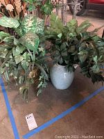 Three planters with faux plants arranged on a concrete floor, showing all plants and planters.